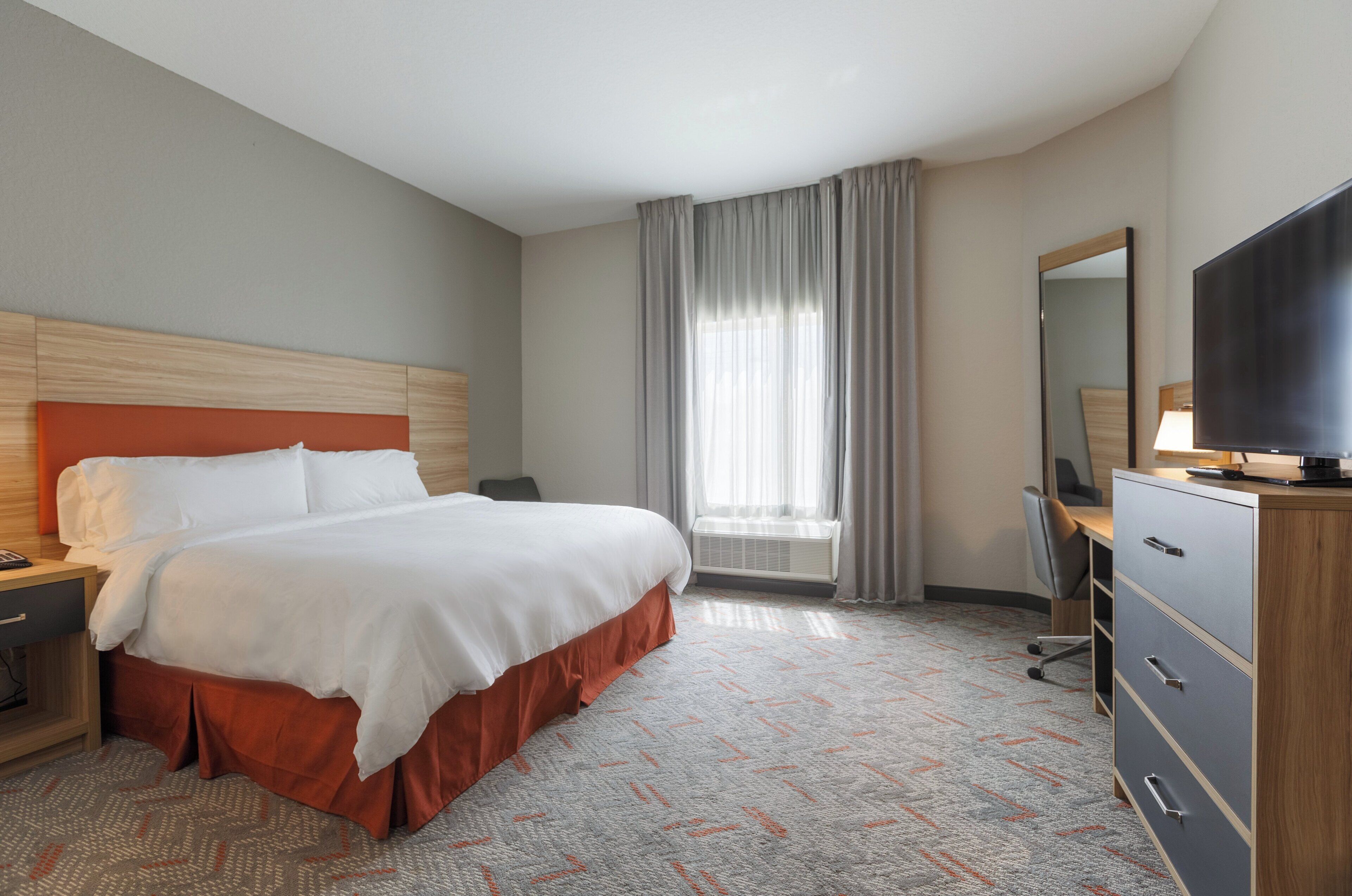 Een hotelkamer met een bed, een bureau, een stoel, een televisie en een raam met gordijnen.