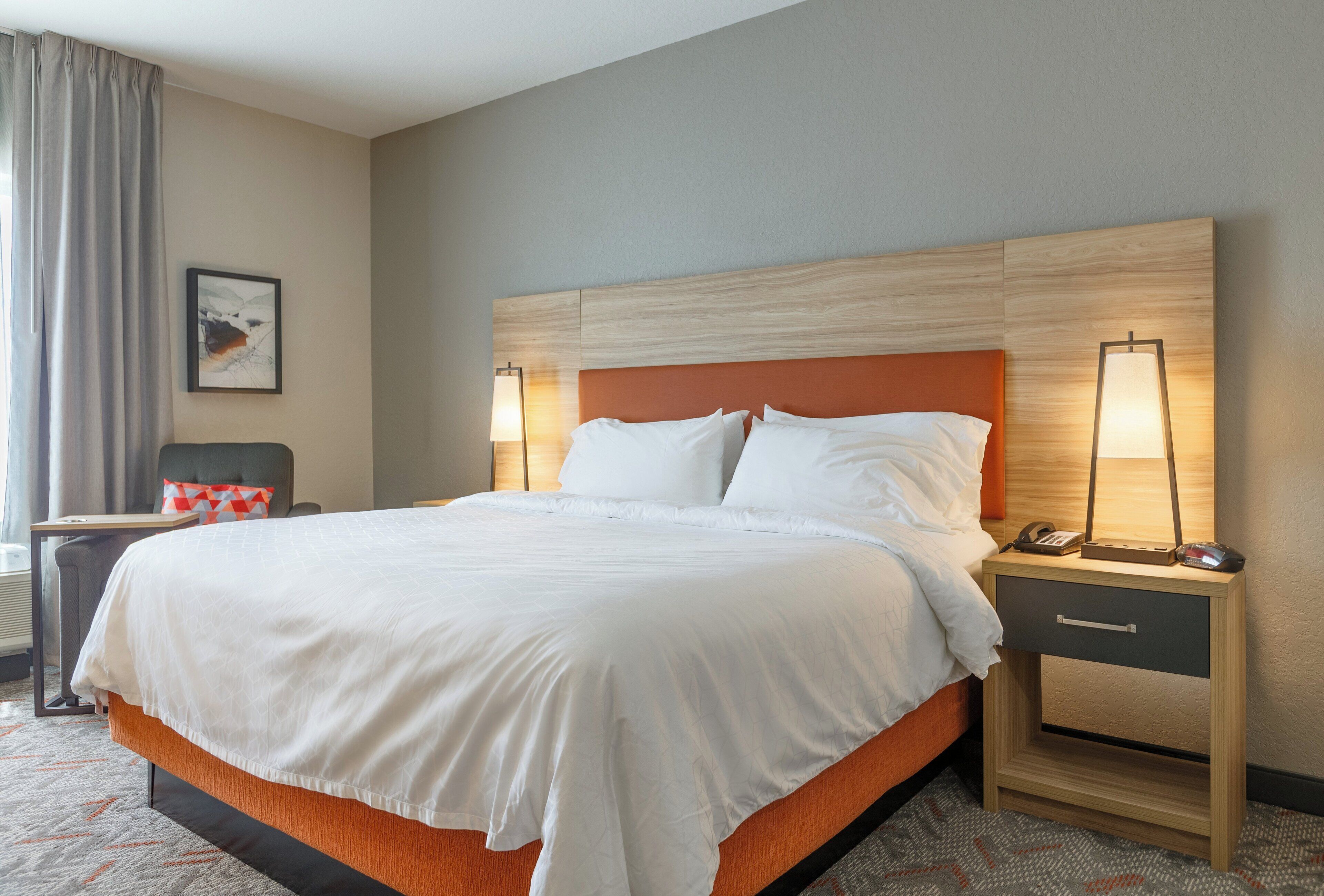 A hotel room with a large bed, two bedside tables, a chair, a lamp, and a painting on the wall.