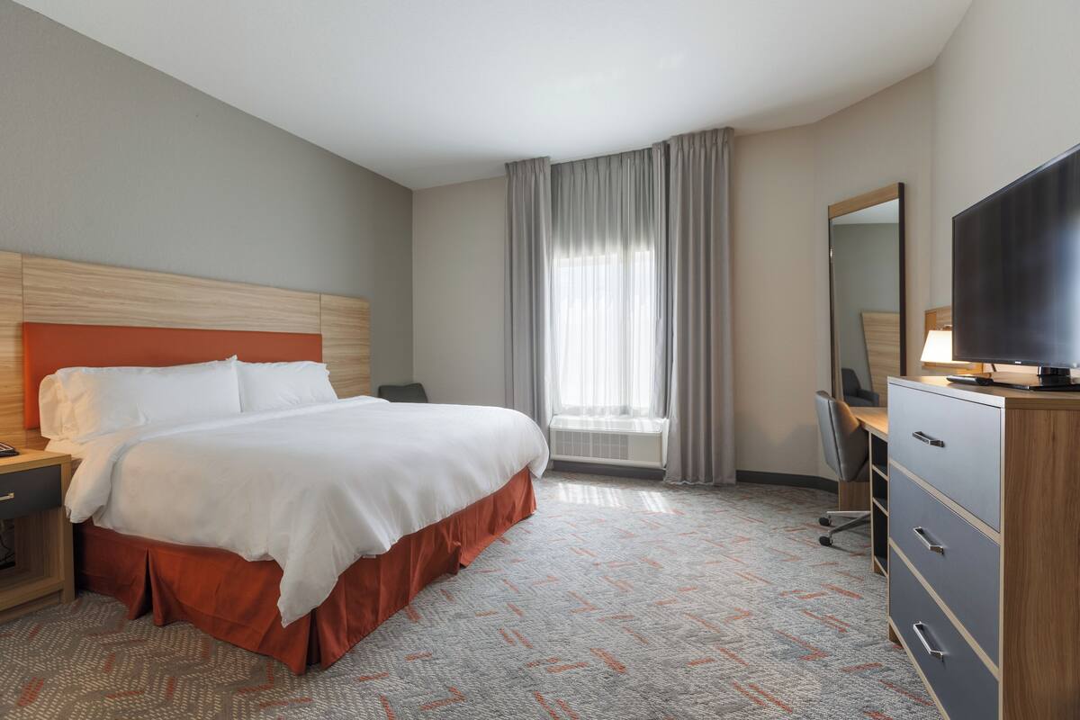 A hotel room with a bed, a desk, a television, and a window with curtains.