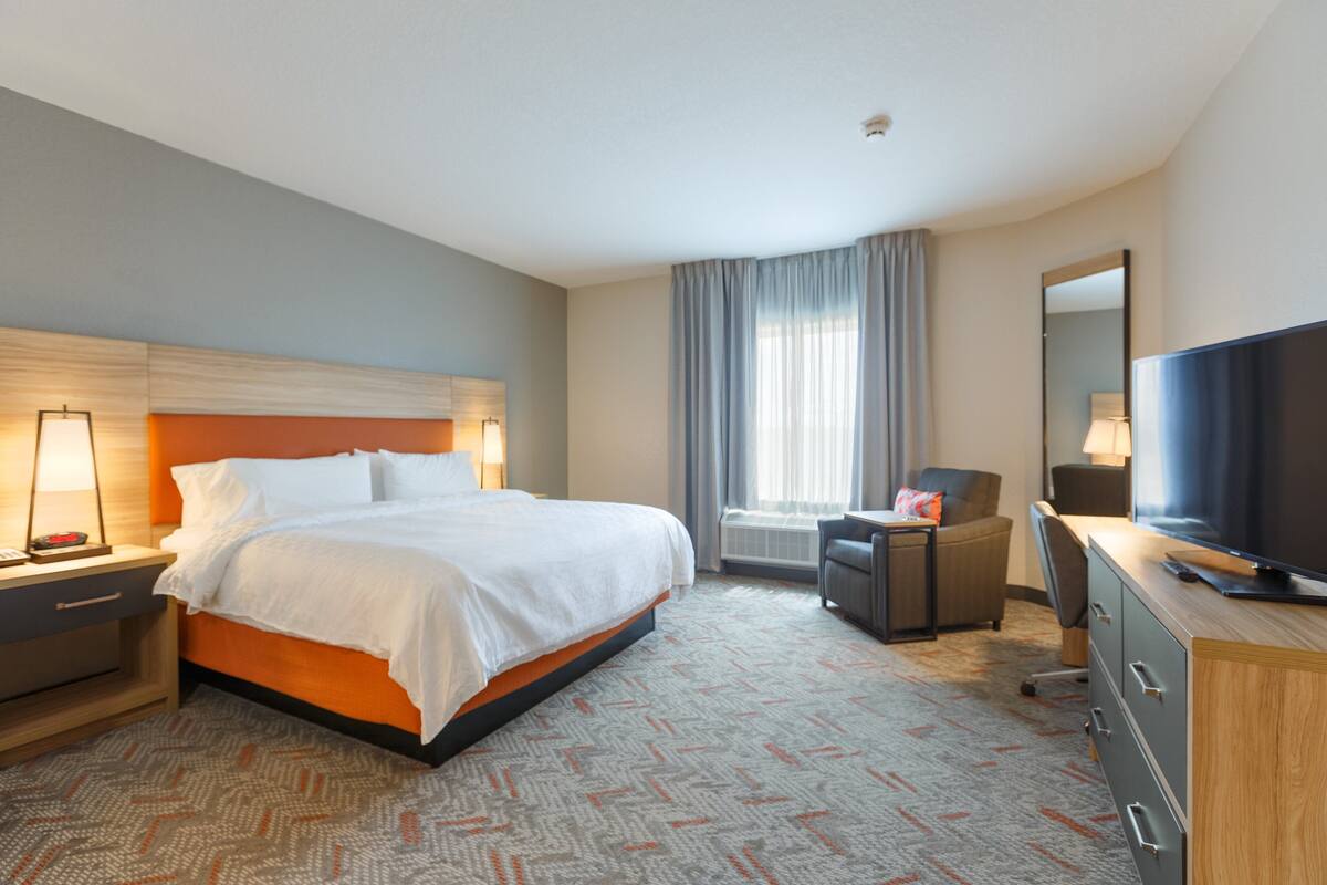 A hotel room with a large bed, a desk with a computer, a TV, and a chair.