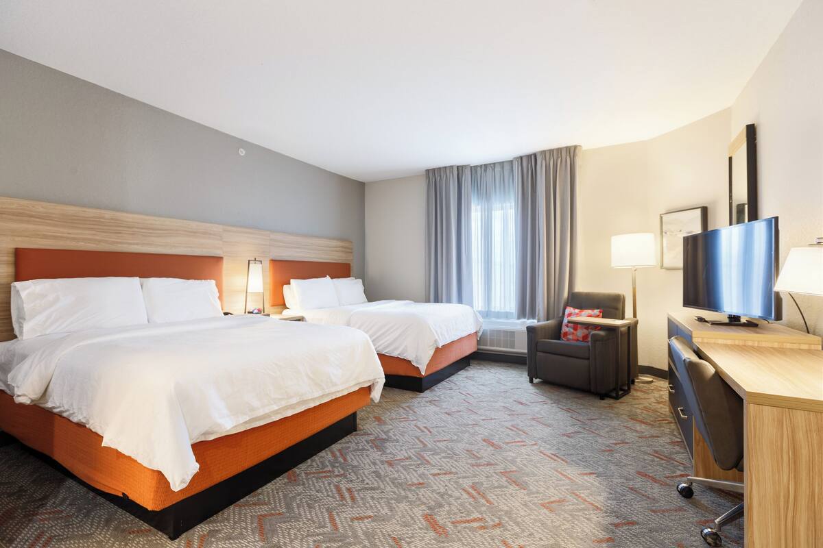 A hotel room with two beds, a desk, a chair, a TV, and a window with curtains.
