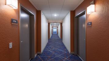Un couloir d'hôtel avec des revêtements de sol en moquette, des portes numérotées et des luminaires fixés au mur.