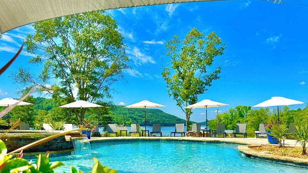 Una piscina con lettini e ombrelloni, immersa nel verde sotto un cielo sereno.
