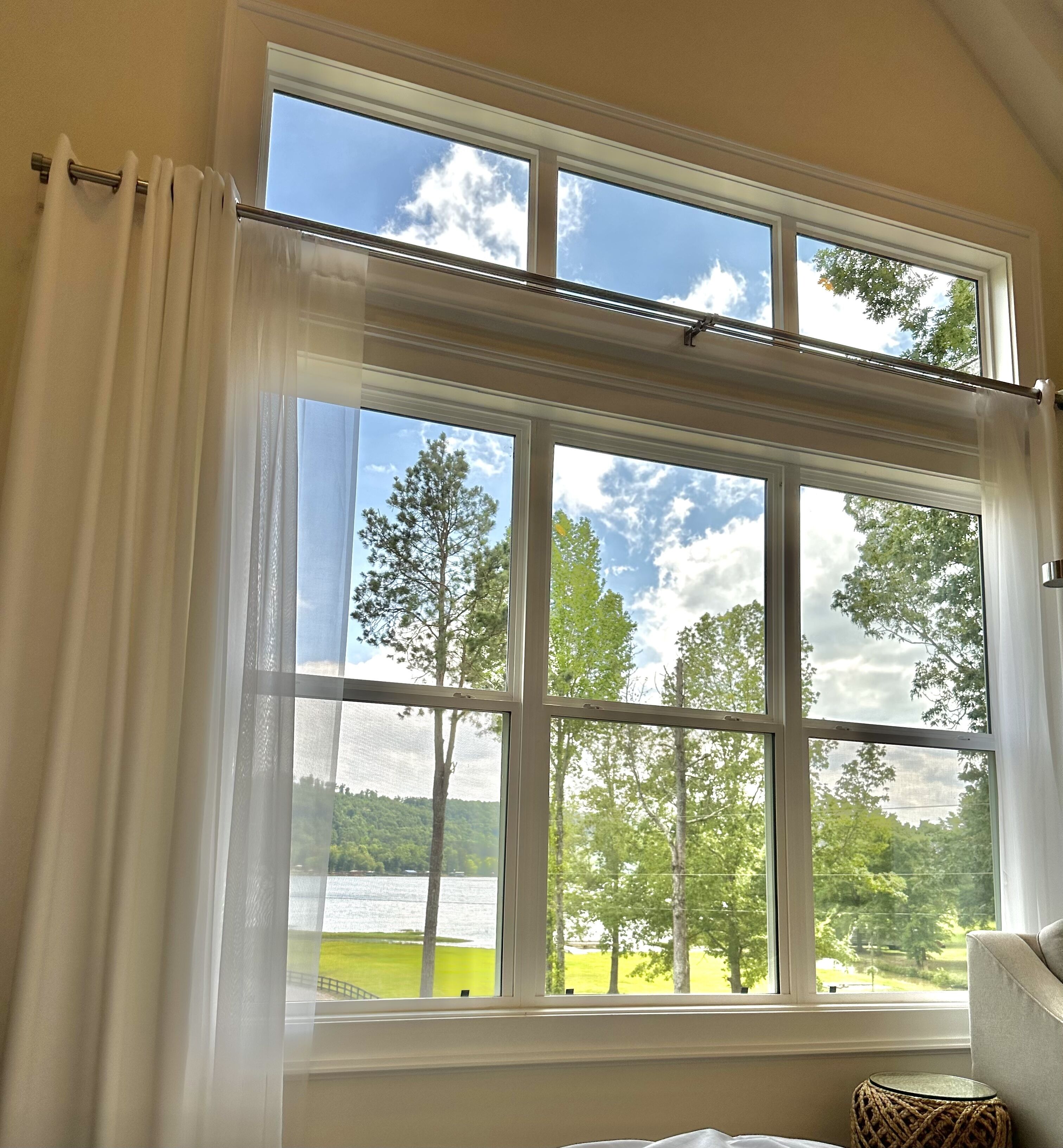 A room with a large window overlooking a lake and trees, with a view of a grassy area and a dock.