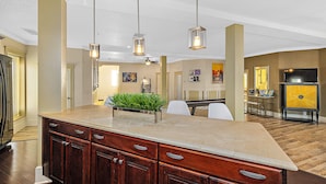A kitchen with a marble countertop, wooden cabinets, pendant lights, and a central island with plants. - The Ray - Penthouse Suite - Rooftop View (St. Augustine)