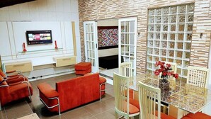 A modern living room with a TV, red sofas, a glass coffee table, and a patterned wall.
