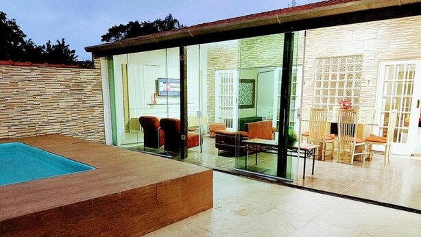 A modern outdoor area with a swimming pool, glass doors leading to a dining area with chairs and tables.
