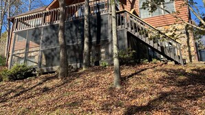A cabin with a wooden exterior, a stone foundation, and a staircase leading to a balcony.