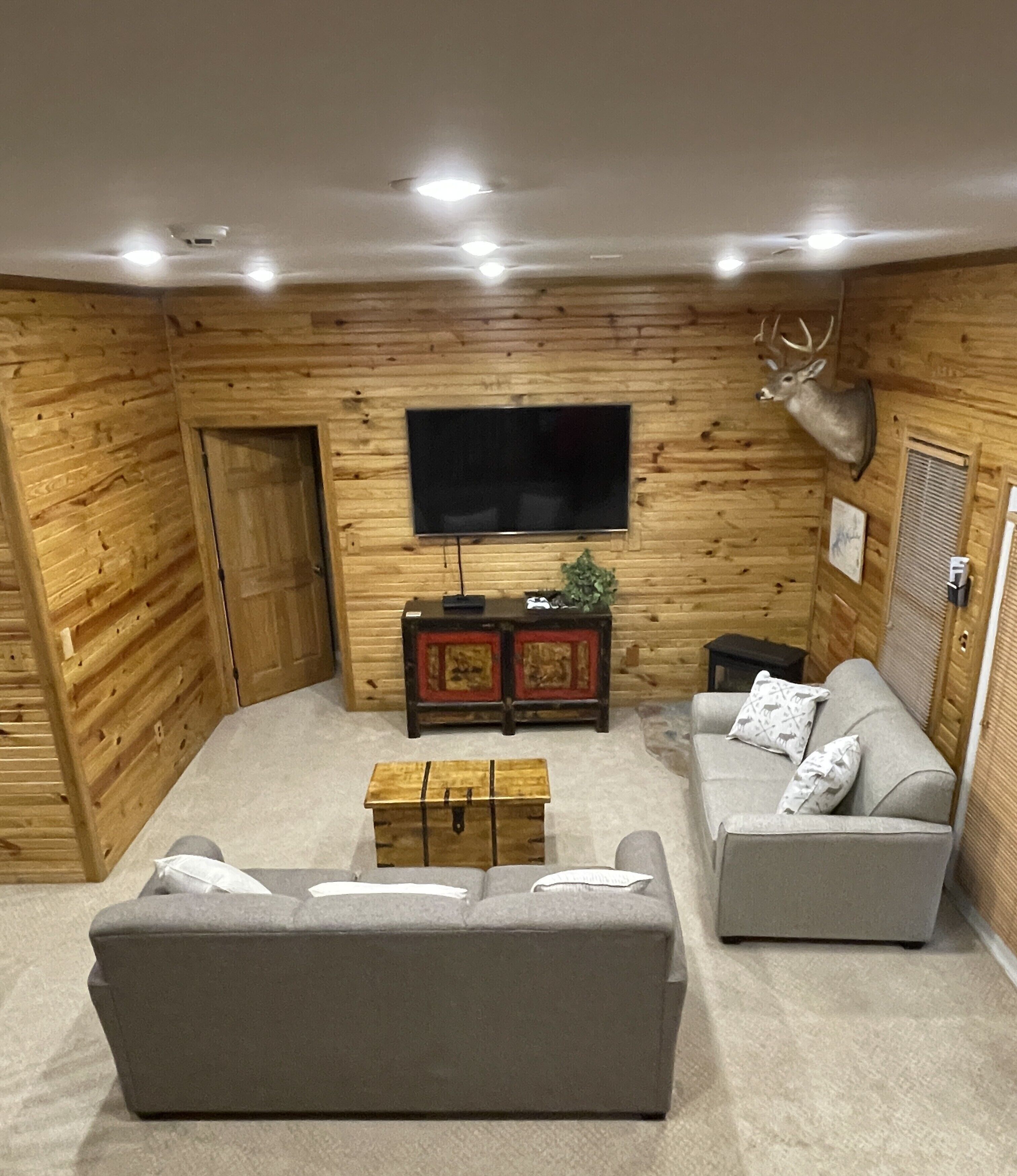 Una sala de estar acogedora con detalles de madera, un televisor de pantalla plana, un sofá, una mesa de centro y una cabeza de ciervo montada en la pared.
