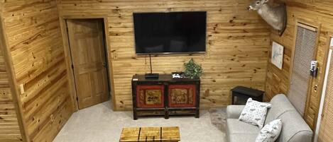 Una sala de estar acogedora con detalles de madera, un televisor de pantalla plana, un sofá, una mesa de centro y una cabeza de ciervo montada en la pared.