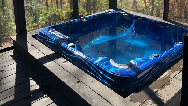 A hot tub on a wooden deck with a view of autumn trees and a clear sky.