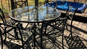 A glass-top table with metal chairs, a blue bench, and a view of trees through large windows.