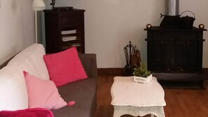 Uma sala de estar com sofá, uma mesa pequena, uma tigela decorativa, um toca-discos antigo e uma lareira a lenha.