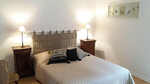 Uma cama bem arrumada com cabeceira acolchoada, duas luminárias de cabeceira e um quadro com pássaros na parede.