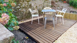 Um pátio externo com deck de madeira, cadeiras de metal branco e uma mesa.