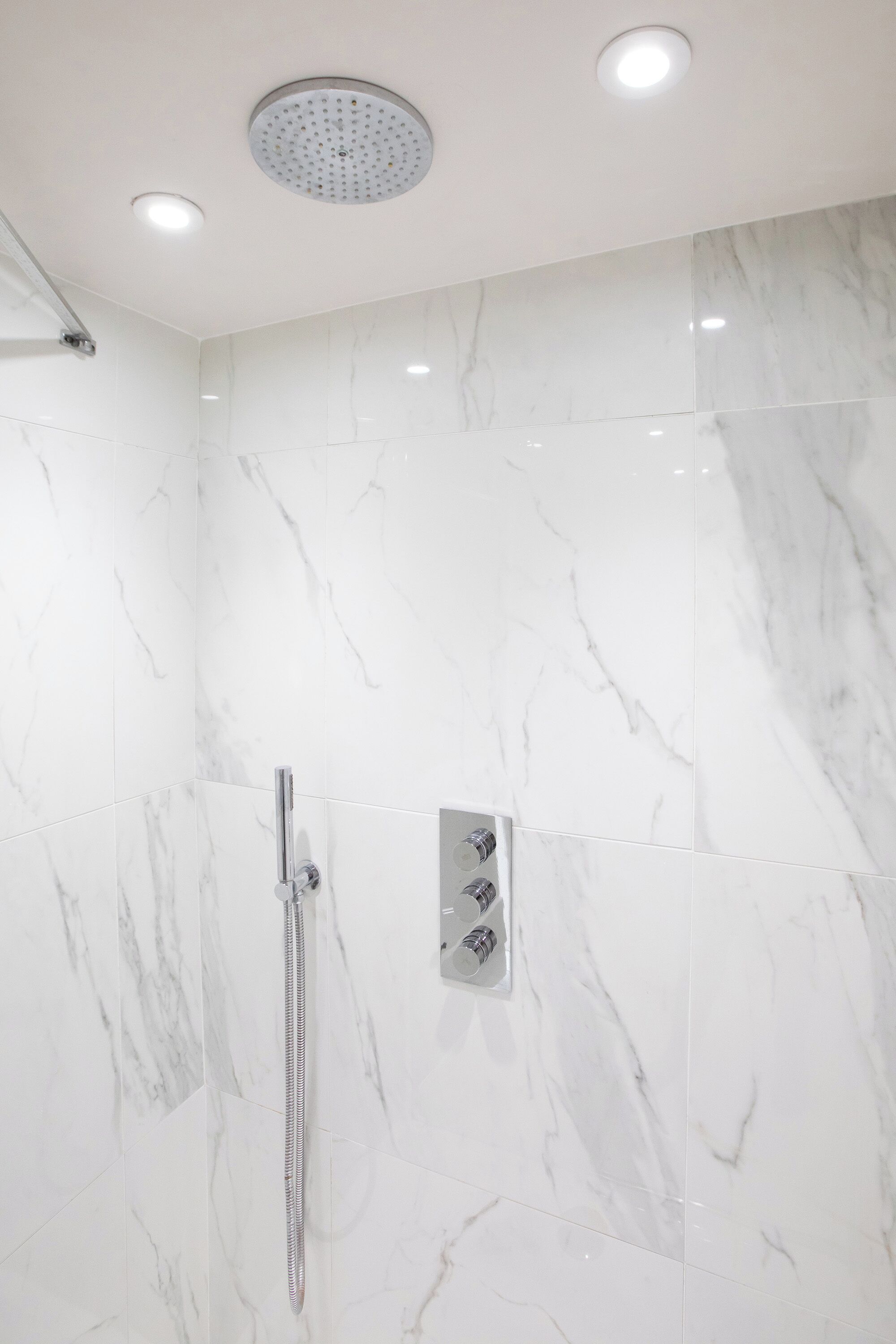 Une douche moderne dotée d’un pommeau de douche à main et d’un panneau de commande fixé au mur.