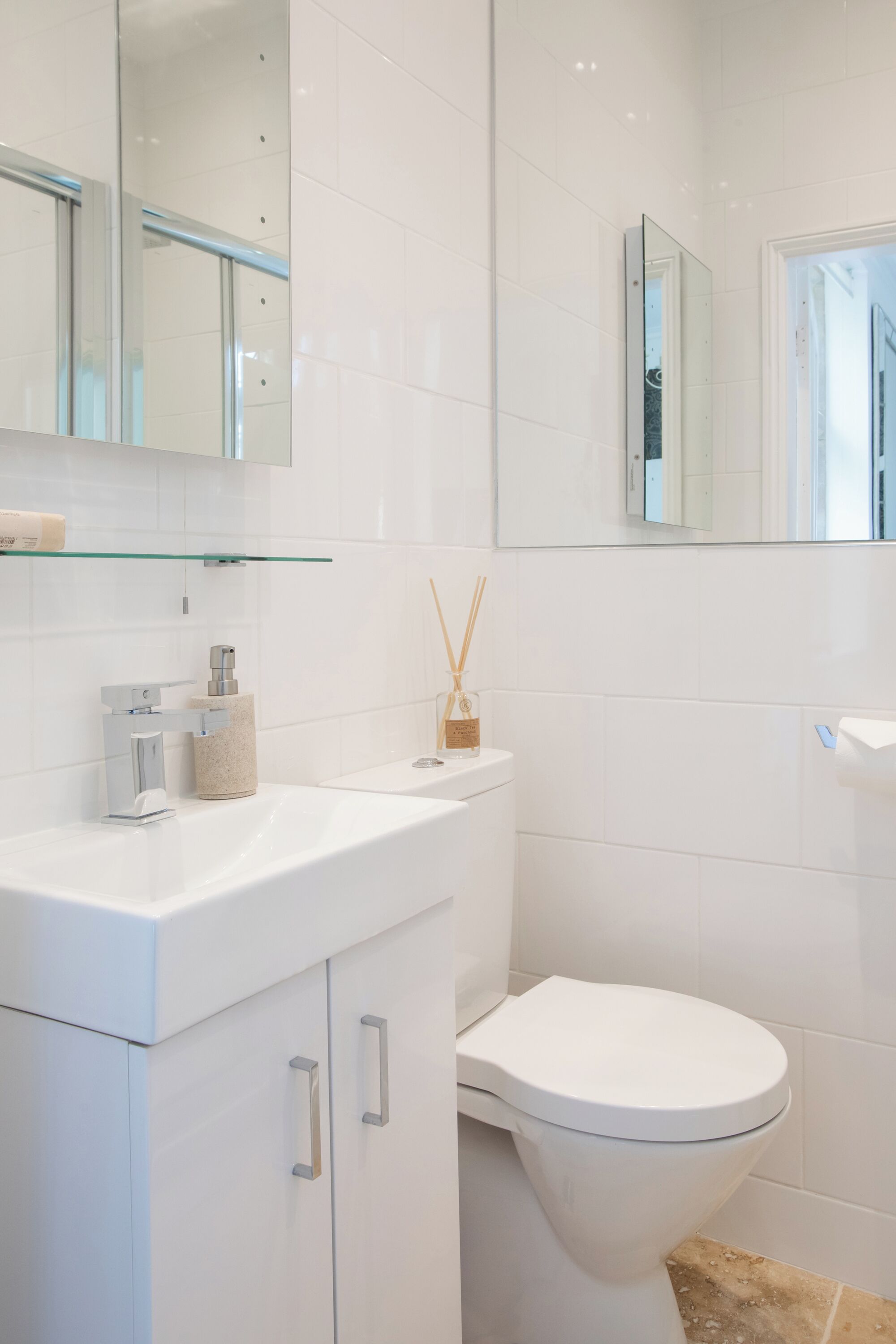 A modern bathroom with a white sink, a toilet, and a glass shelf above the sink.
