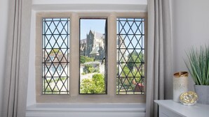 A window with a metal grid, curtains, and a view of a church and greenery. - Beautiful Iconic Listed Building with Views Overlooking the Arundel Cathedral (Arundel)