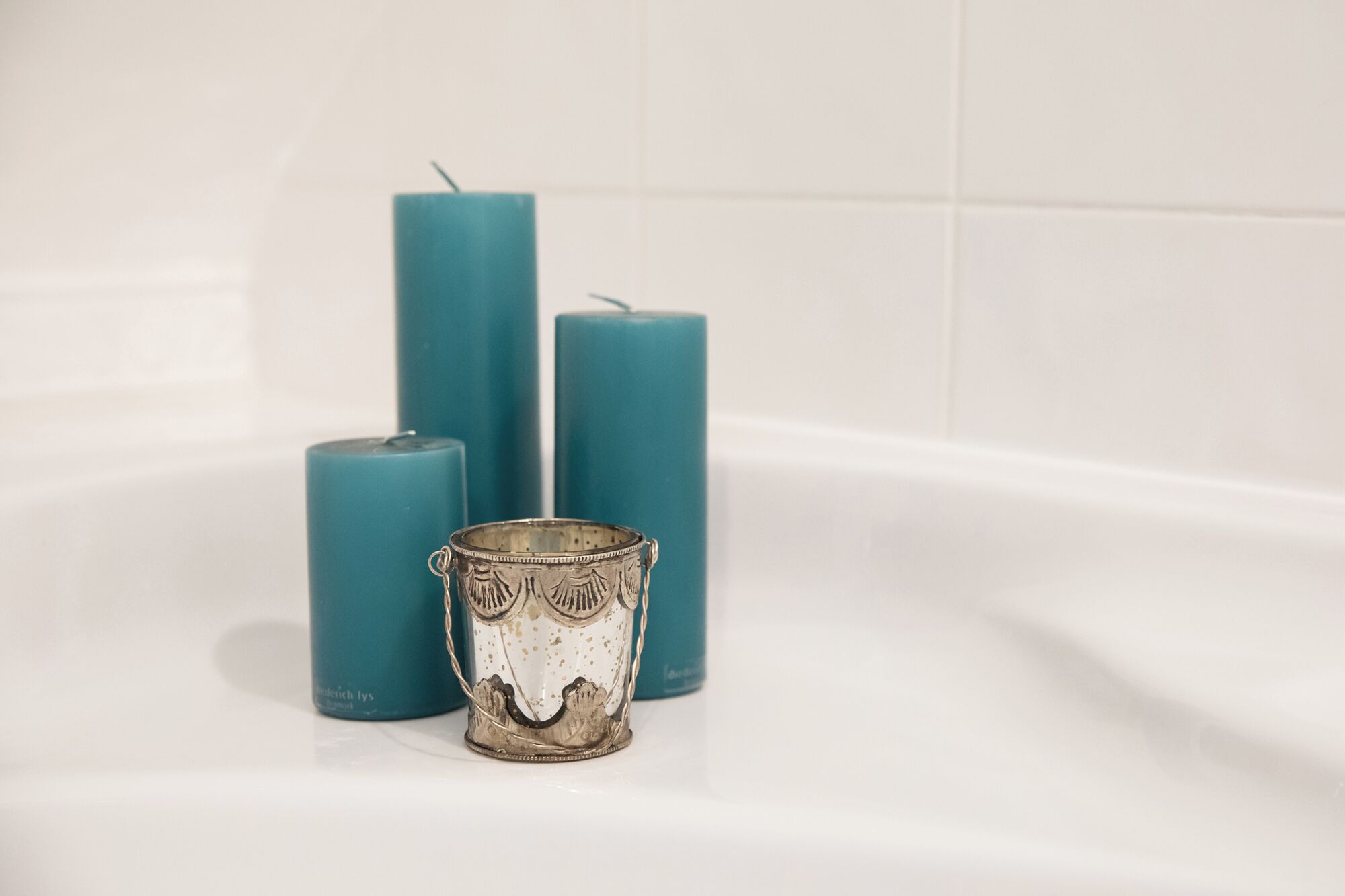 Tres velas color turquesa y un candelabro metálico sobre una superficie blanca.