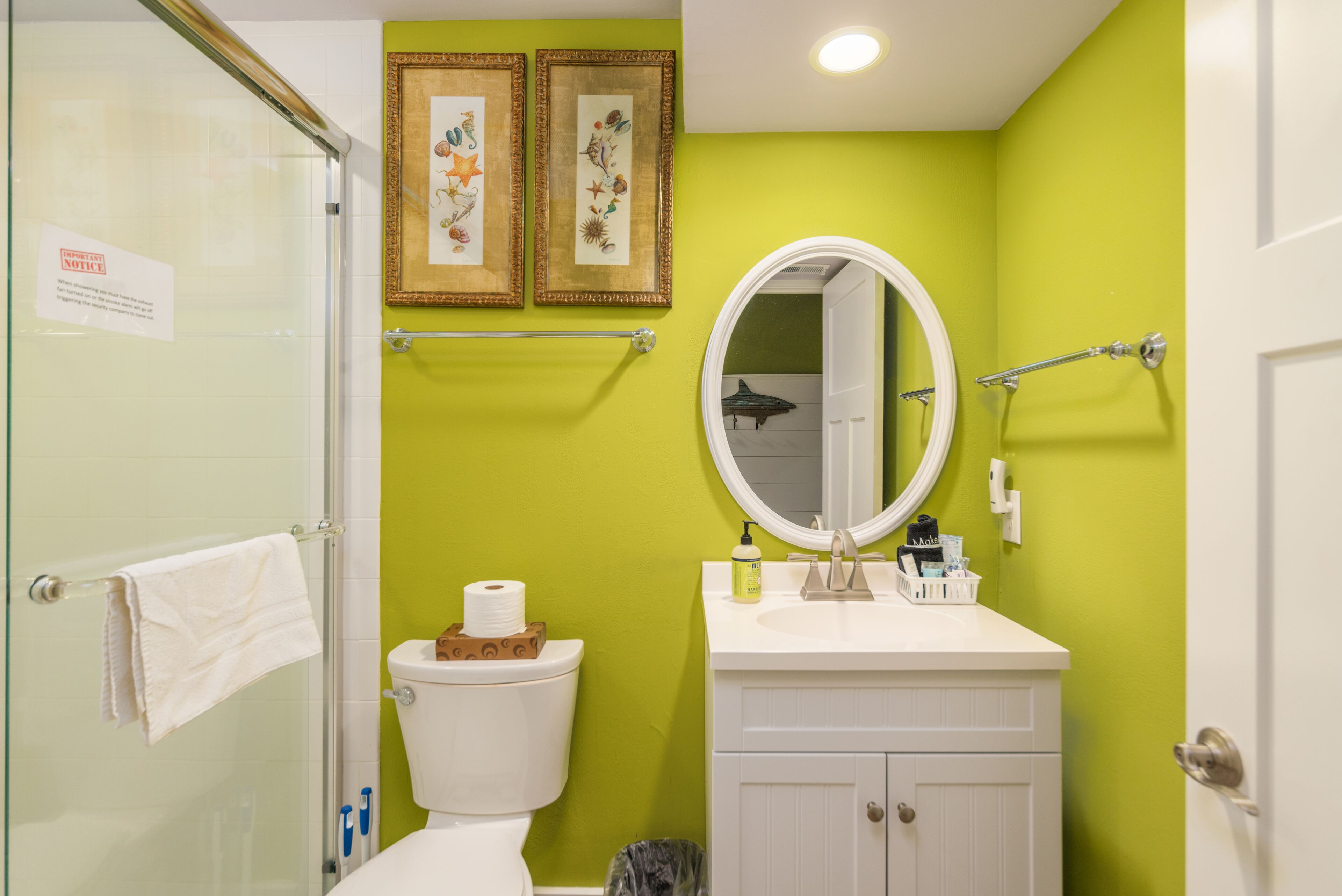 Un baño con inodoro, lavabo y ducha. Hay cuadros enmarcados en la pared y un espejo sobre el lavabo.