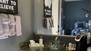 A bathroom with a large mirror, a glass sink, wooden cabinets, and towels on a rack. - UnWIned Arizona (Litchfield Park)
