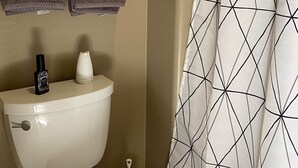 A bathroom with a toilet, two towels, and a geometric-patterned shower curtain. - UnWIned Arizona (Litchfield Park)