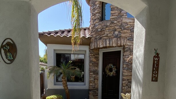 A stone house with a welcoming archway, a door with a wreath, and a pathway leading to the entrance. - UnWIned Arizona (Litchfield Park)