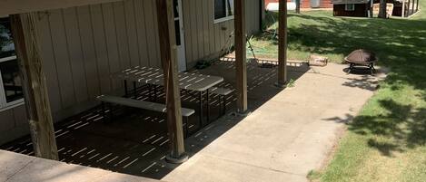 A covered patio area with a stone bench, a grill, and a wooden deck.