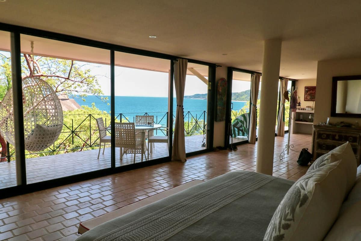Ein Schlafzimmer mit großem Bett, Meerblick und einem Balkon mit Sitzmöbeln.