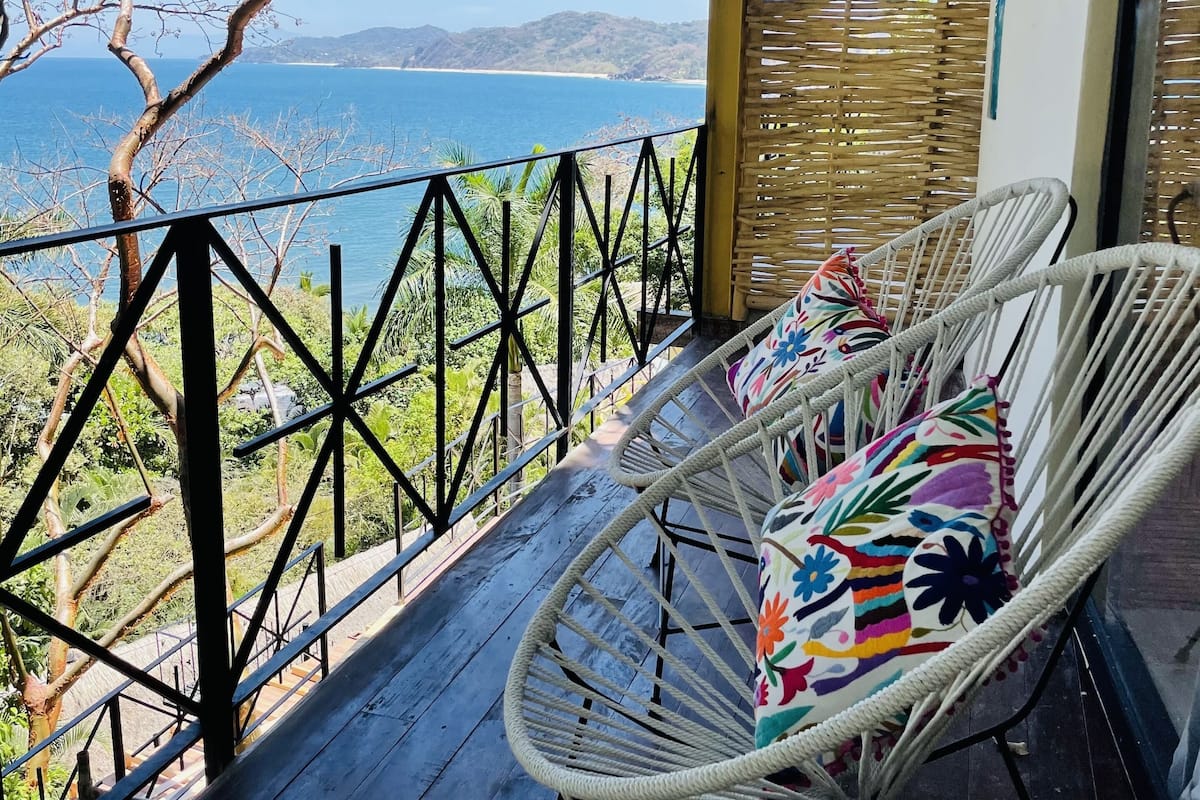 Ein Balkon mit Korbstühlen und Blick auf das Meer.