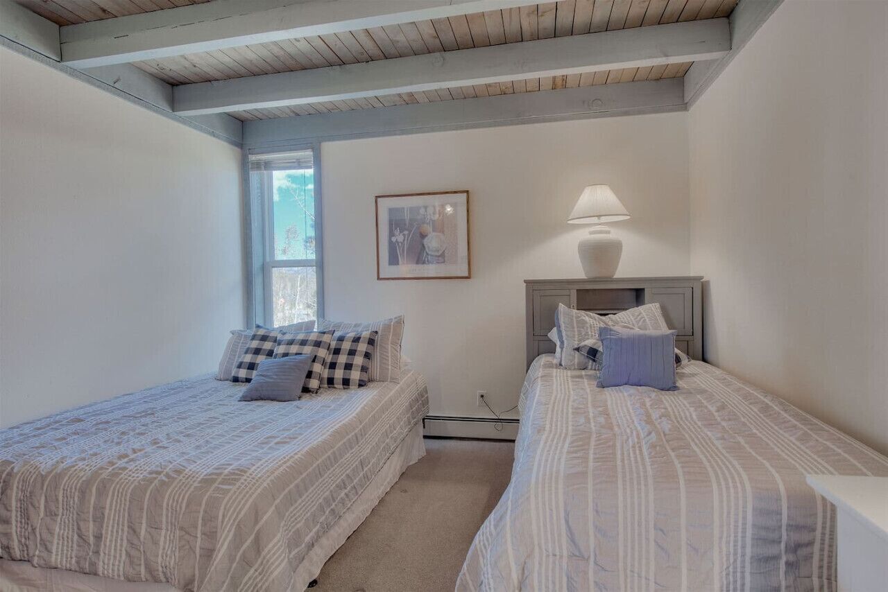 A bedroom with two beds, a window, a framed picture, and a bedside lamp.