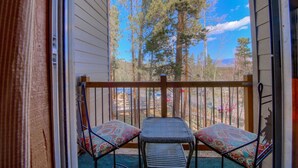 A balcony with two wicker chairs and a small table, overlooking a forested area.