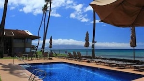 A swimming pool with lounge chairs and umbrellas, overlooking a beach with palm trees. - Hale Kai #116 Direct Oceanfront Condo, just steps to the beach, pool and BBQ! (Lahaina)