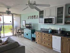 Une cuisine de taille réduite avec des meubles de couleur turquoise, un lave-vaisselle blanc et un ventilateur de plafond.