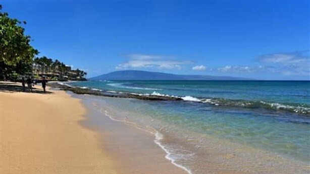 A beach with clear blue water, a sandy shore, and a distant mountain. - Hale Kai #116 Direct Oceanfront Condo, just steps to the beach, pool and BBQ! (Lahaina)