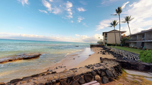 A beach with a stone wall and a building with a balcony overlooking the ocean.