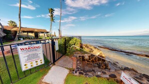 A beachside property with a warning sign about ocean conditions, a pool, and a view of the ocean. - Hale Kai #116 Direct Oceanfront Condo, just steps to the beach, pool and BBQ! (Lahaina)