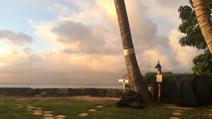 A grassy area with a stone path leading to a beach, palm trees, and a small structure with a sign. - Hale Kai #116 Direct Oceanfront Condo, just steps to the beach, pool and BBQ! (Lahaina)