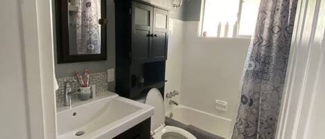 A bathroom with a white sink, dark cabinets, a toilet, a shower with a patterned curtain, and a ceiling light.
