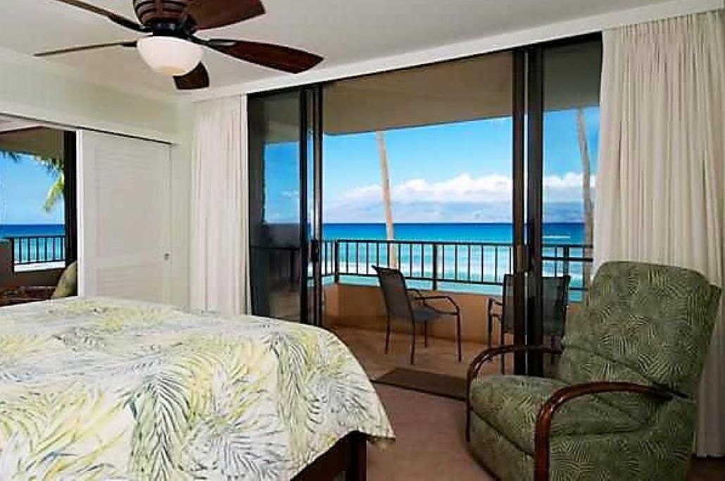 A hotel room with a bed, a chair, and a balcony with a view of the ocean.