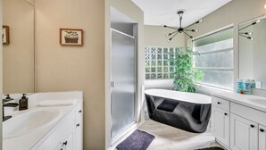 A modern bathroom with a white vanity, a freestanding bathtub, a large mirror, and a potted plant.