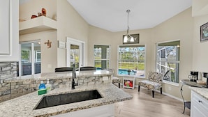 A spacious kitchen with granite countertops, a large island, and a view of a swimming pool.