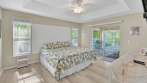 A bedroom with a bed, ceiling fan, and a view of the outside.