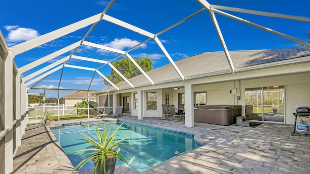 A covered outdoor swimming pool with a patio area, seating, and a hot tub.