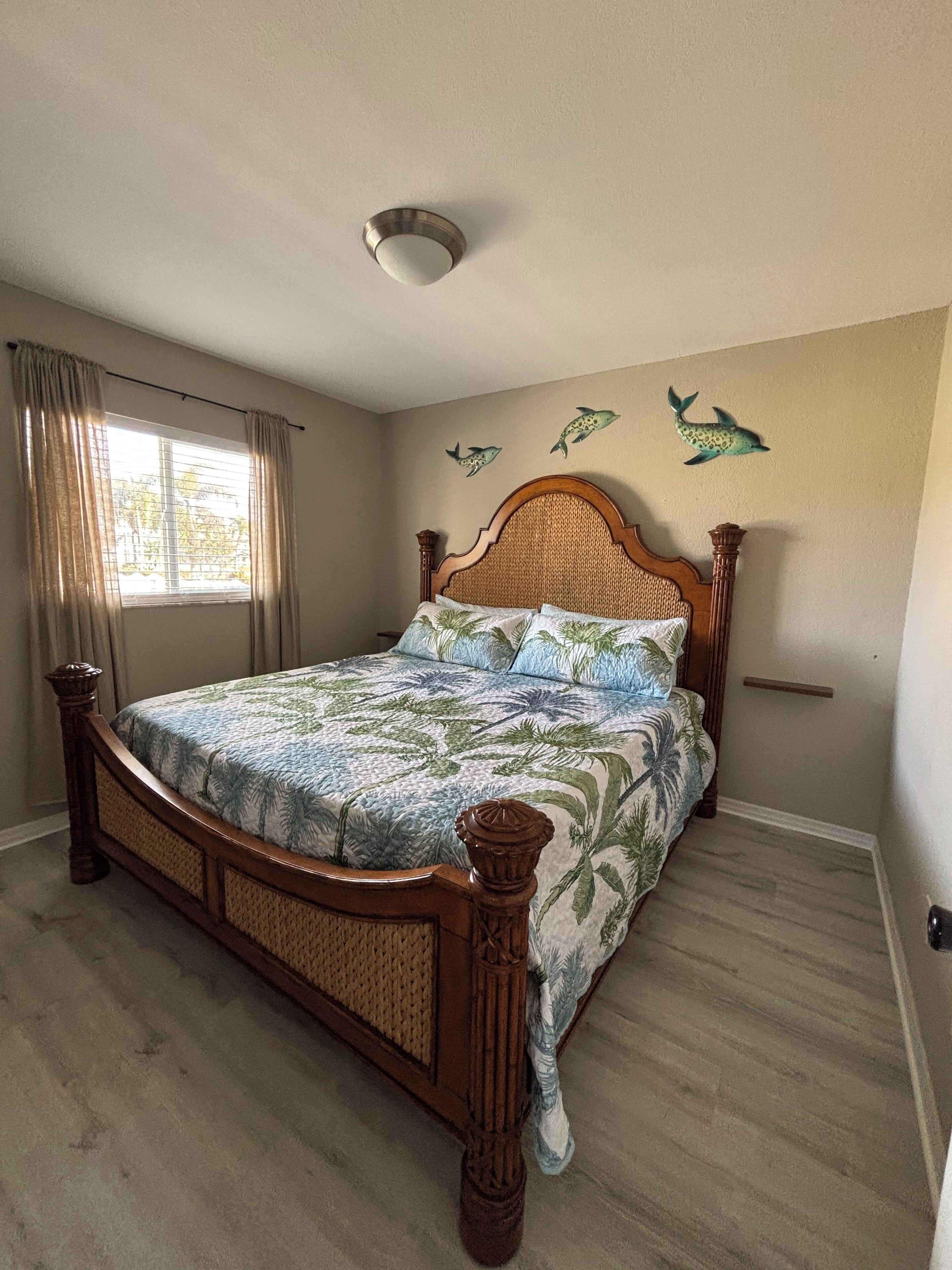 A bedroom with a wooden bed, a window with curtains, and wall art of dolphins.
