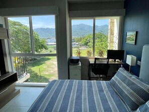 A bedroom with a large bed, a desk with a computer, and a view of a mountainous landscape.