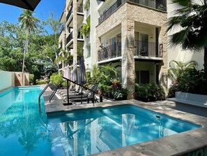 A swimming pool with a metal ladder, lounge chairs, and a stone building with balconies.