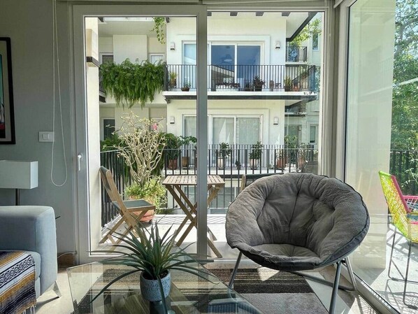 A modern living room with a glass door leading to a balcony, a grey armchair, a small table, and a potted plant.
