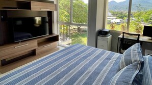 Une chambre avec un grand lit, une télévision, un bureau avec un ordinateur et une vue sur la verdure et les montagnes.