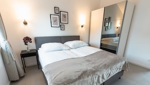 A modern bedroom with a large bed, a nightstand, a vase of flowers, and framed pictures on the wall. - Ostseehaus am Naturstrand - Ostseeblick (Putgarten)